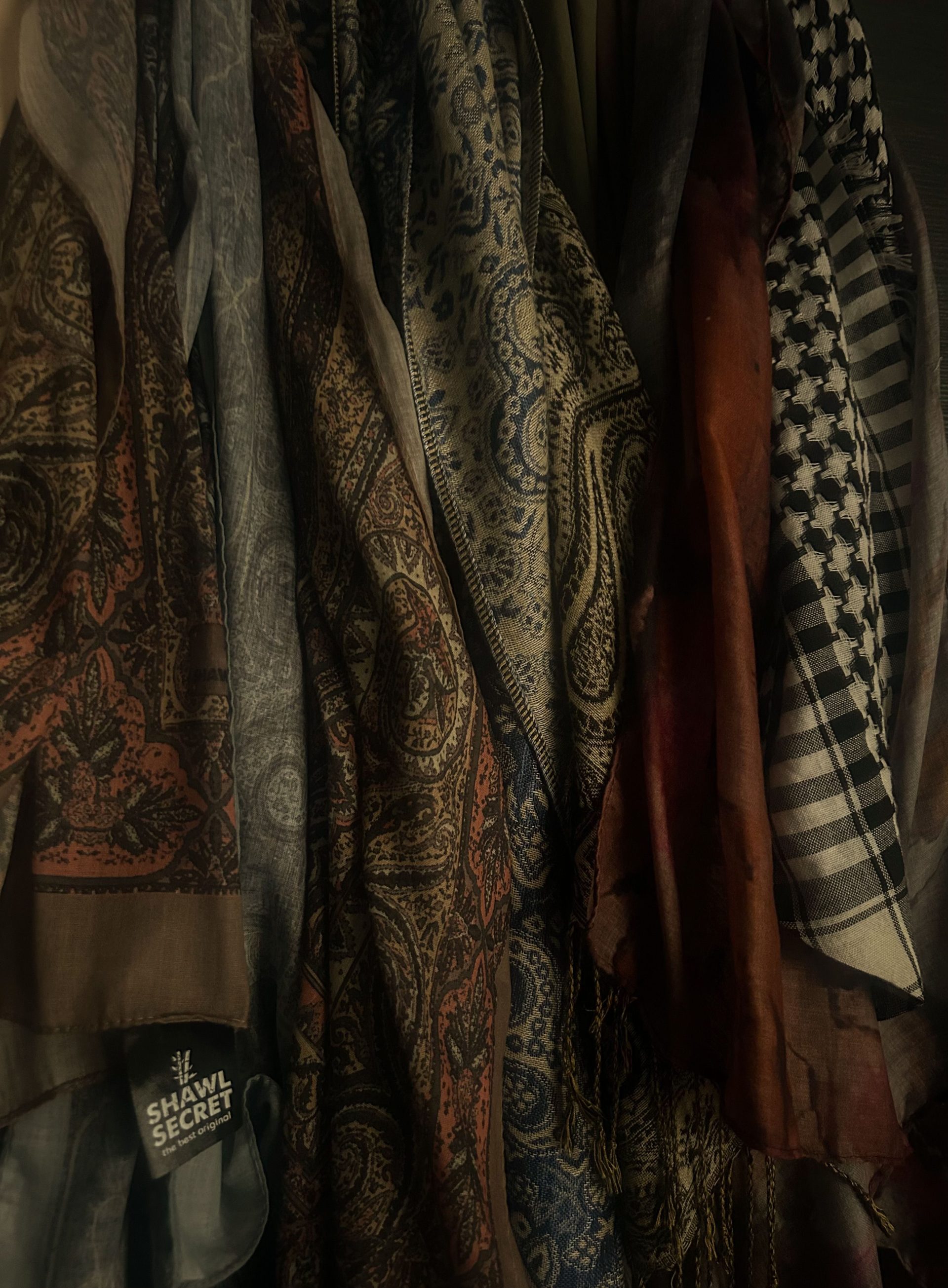 Intricately patterned scarves hanging in a dim light, showcasing cultural textile design.